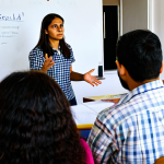 **

A diverse group of adults and teenagers participate in a community safety workshop in a brightly lit neighborhood center in Madrid. The facilitator, a woman in her 40s wearing a professional blouse, gestures toward a whiteboard displaying the words "Convivencia y Seguridad" (Coexistence and Security). Participants are engaged in discussions at tables, reviewing pamphlets about local crime prevention programs. The atmosphere is positive and collaborative. Include elements of a typical Spanish barrio, like posters promoting local events. Focus on capturing the sense of community and proactive engagement.  "Safe for work", "appropriate content", "fully clothed", "professional", "family-friendly". perfect anatomy, correct proportions, natural pose, well-formed hands, proper finger count, natural body proportions.
**